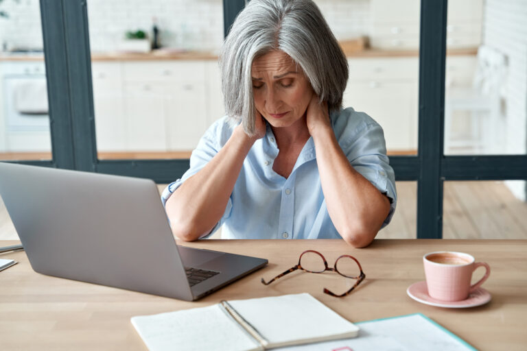 older woman in pain sat at desk holding neck