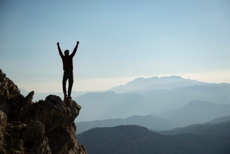 Person standing on top of mountain with arms up in celebration